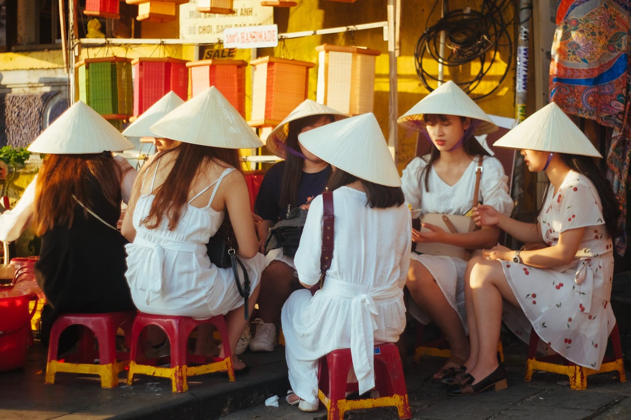 Women wearing traditional conical hats gather outdoors, enjoying leisure time on a sunny day.